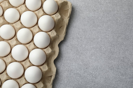 Raw chicken eggs in egg carton on gray table, top view. Space for text