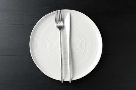 Clean ceramic plate and cutlery on black wooden table, top viewの写真素材