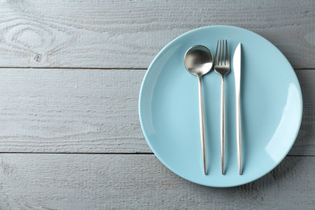 Clean ceramic plate and cutlery on wooden table, top view. Space for textの写真素材
