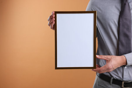 Man with diploma blank frame on pale orange background, closeup. Mockup for designの写真素材