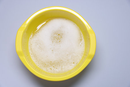 Yellow plastic basin with water and foam on gray background, top viewの写真素材