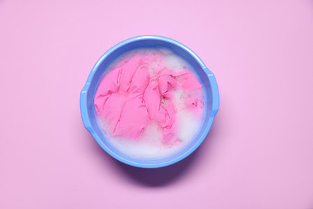 Plastic basin with clothes, water and foam on pink background, top viewの写真素材