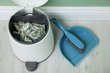 Dollar banknotes in trash bin, dustpan and broom on floor, above viewの写真素材