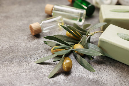 Handmade soap bars, olives, green leaves on gray textured table, closeup. Space for text