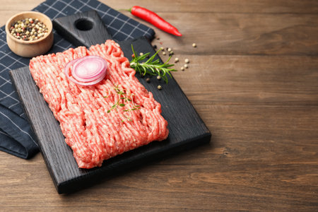 Raw minced meat with rosemary, thyme and spices on wooden table, closeup. Space for text