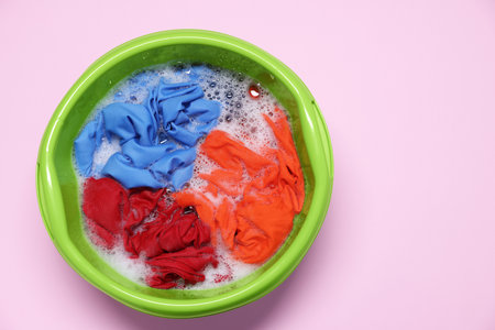 Plastic basin with clothes, water and foam on pink background, top viewの写真素材