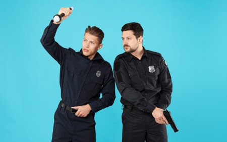Policemen in uniform with gun and flashlight on light blue backgroundの写真素材