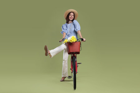 Smiling woman in hat and bicycle with basket of flowers on green background