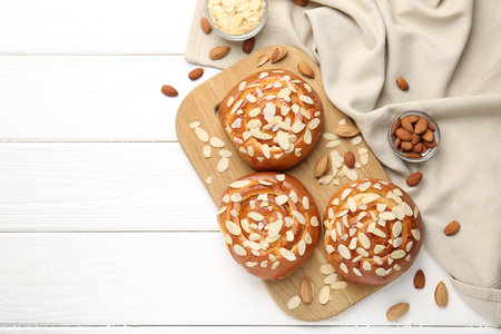 Tasty roll buns with almond flakes and nuts on white wooden table, flat lay. Space for textの写真素材