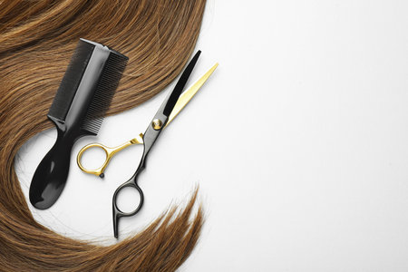 Beautiful brown hair, scissors and comb on white background, top view. Space for textの写真素材