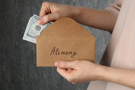 Alimony. Woman taking money from envelope on gray background, closeupの写真素材