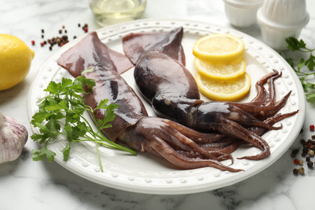 Raw squids, lemon and other products on white marble table, closeup
