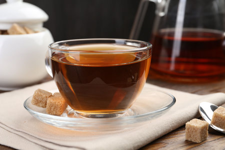 Aromatic black tea in glass cup, brown sugar and teapot on wooden table, closeupの写真素材