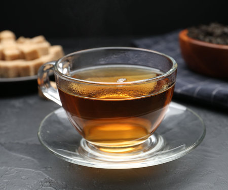 Aromatic tea in glass cup, brown sugar and dried leaves on black table, closeupの写真素材