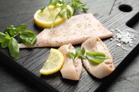 Pieces of raw squid, lemon and herbs on black table, closeupの写真素材