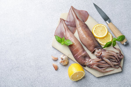 Raw squids, lemon, knife, garlic and basil on light gray table, flat lay. Space for textの写真素材