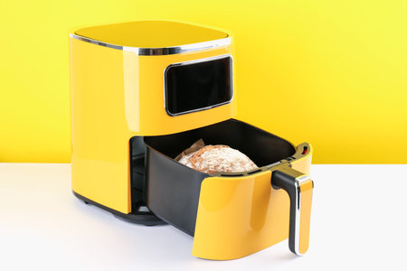 Air fryer with baked bread on white table against yellow background