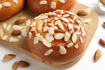 Tasty roll buns with almond flakes and nuts on white wooden table, closeup