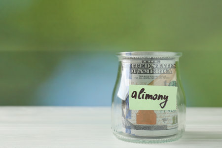 Jar with word Alimony and money on white wooden table against blurred background. Space for textの写真素材