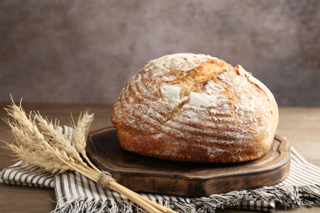 Loaf of fresh bread and spikes on wooden table, closeup