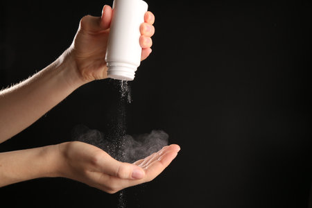 Woman with talcum powder on black background, closeup. Space for textの写真素材