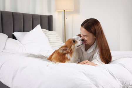 Happy woman with her cute Welsh Corgi dog lying on bed indoorsの写真素材