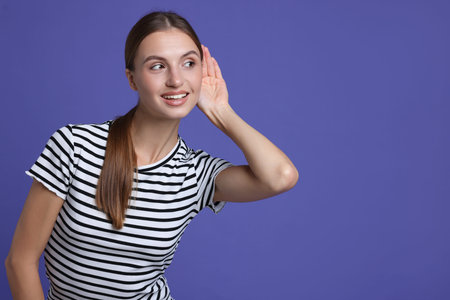 Woman showing hand to ear gesture on purple background, space for text