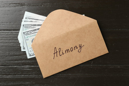 Envelope with word Alimony and money on wooden table, flat lay