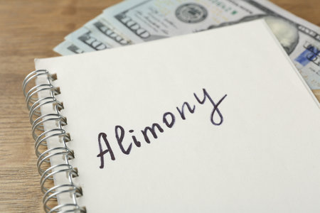 Notebook with word alimony and money on wooden table, closeupの写真素材