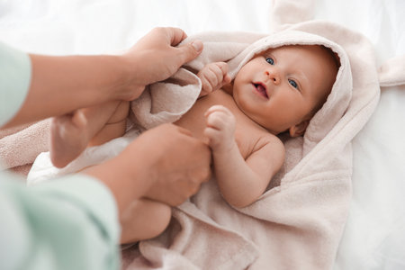 Mother covering her baby with towel after bathing on bed, closeupの写真素材