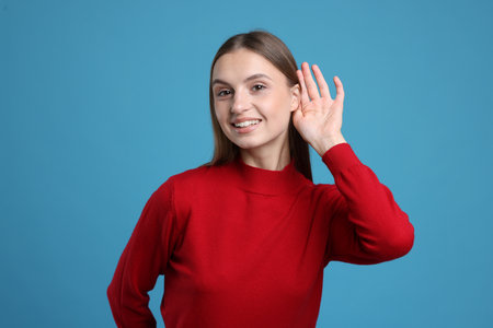 Woman showing hand to ear gesture on light blue backgroundの写真素材