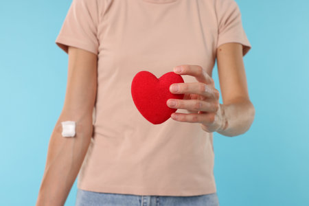 Blood donation. Woman with bandage on arm and decorative heart against light blue background, closeupの写真素材