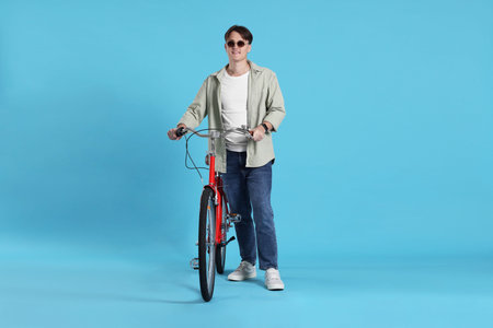 Handsome man with red bicycle on light blue background