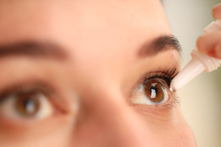 Woman applying eye drops on blurred background, closeupの写真素材