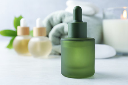 Essential oils, towel, spa stones, burning candle and green leaves on white table, closeup. Space for textの写真素材