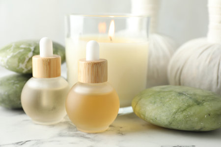Beautiful spa composition with essential oils and burning candle on white marble table, closeupの写真素材