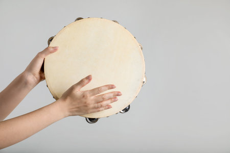 Woman playing tambourine on light background, closeupの写真素材