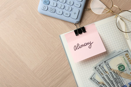 Note with word Alimony, money, notebook, calculator and glasses on wooden table, flat lay. Space for textの写真素材