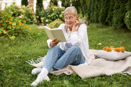 Senior woman reading book on blanket in gardenの写真素材