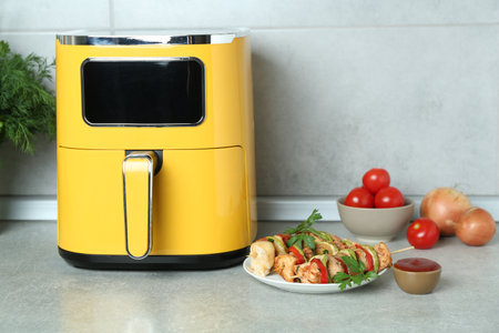 Tasty skewers with chicken, vegetables, parsley, sauce and air fryer on light countertop. Space for textの写真素材