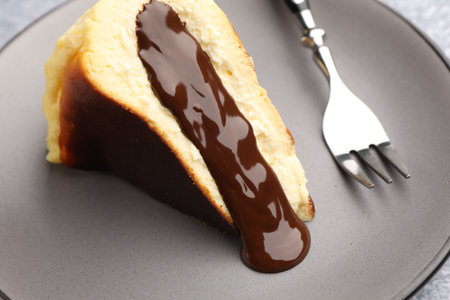 Piece of delicious Basque cheesecake with chocolate sauce and fork on plate, closeup