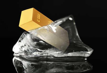 Gold bar in melting ice cube on black background.