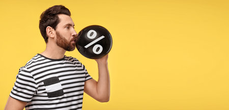 Man blowing black balloon with percent sign on orange background. Discount offerの写真素材