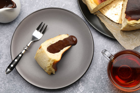 Delicious Basque cheesecake with chocolate sauce, tea and fork on gray table, flat layの写真素材