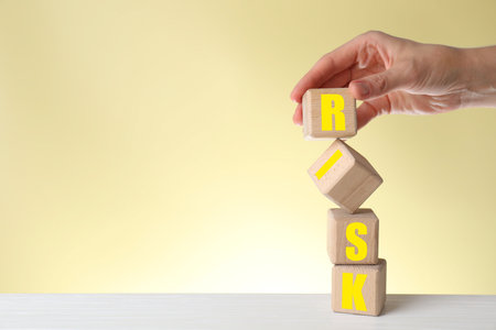 Woman making word Risk of wooden cubes at table against beige background, closeup
