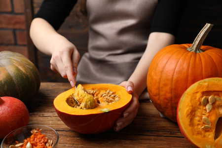 Woman removing seeds from raw pumpkin at wooden table, closeupの写真素材