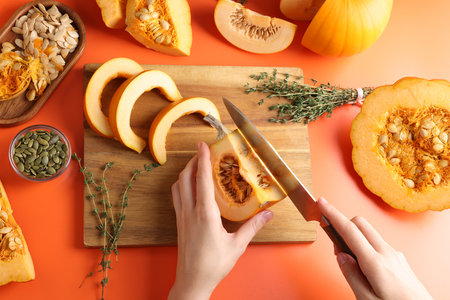 Woman cutting pumpkin on orange background, above viewの写真素材