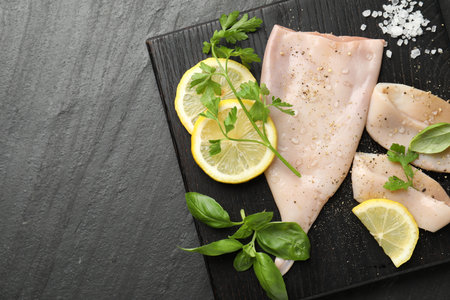 Pieces of raw squid, lemon and herbs on black table, top view. Space for textの写真素材