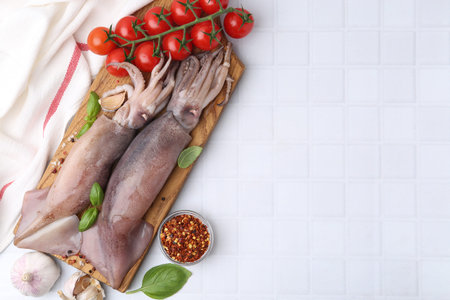 Fresh raw squids, tomatoes and spices on white tiled table, top view. Space for text