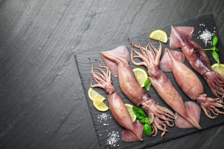 Raw squids, lemon and basil on black table, top view. Space for text
